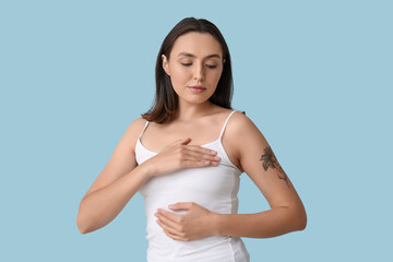 Young woman checking her breast on blue background. Cancer awareness concept