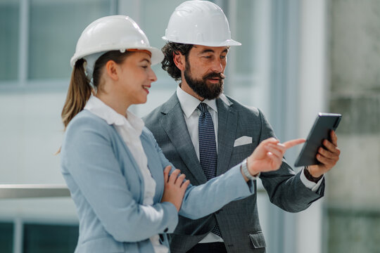 Architects using digital tablet discussing blueprint in modern building - Powered by Adobe