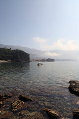 Crystal waters and mountain majesty: a panoramic view of Budva framed by the sea and distant peaks. Boat against the backdrop of the old town.