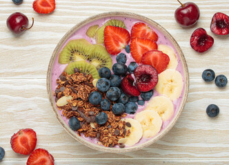 Vibrant acai bowl topped with fresh fruits like bananas, strawberries, kiwi, blueberries, cherries, crunchy granola for a healthy meal, breakfast or snack