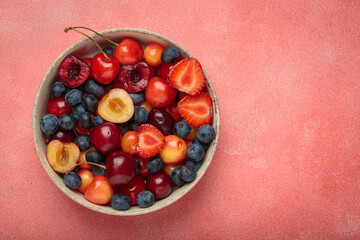 Simple, healthy, and delicious mix of fresh summer fruits is presented in a bowl, sitting on a textured pink background top view