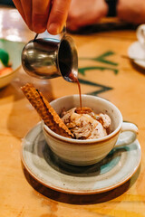 Pouring hot sauce over ice cream in a cozy cafe during a delightful afternoon treat