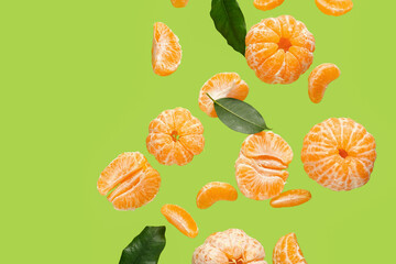 Flying sweet peeled mandarins and leaves on green background