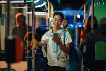 Young woman listening to music on bus while using smartphone