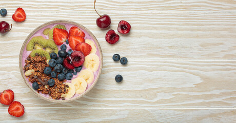 Vibrant acai bowl topped with fresh fruits like bananas, strawberries, kiwi, blueberries, cherries, crunchy granola for a healthy meal, breakfast or snack, copy space