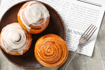 Plate with cinnamon buns, fork and newspaper on grey grunge background