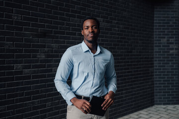 Confident businessman holding notebook by black brick wall