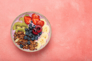 Vibrant and nutritious acai bowl topped with sliced kiwi, strawberries, blueberries, cherries, banana, and granola, a colorful and healthy meal or breakfast on a pink background, copy space