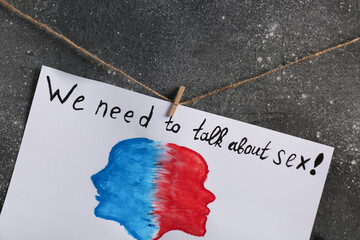Paper sheet with drawn faces and text WE NEED TO TALK ABOUT SEX on dark background. Sex education