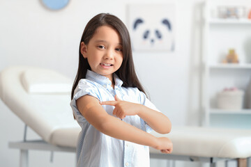 Little Asian girl pointing at applied patch after vaccination in clinic