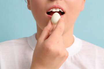 Young woman with fresh boiled quail egg on blue background, closeup