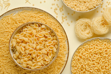 Bowls with different types of delicious uncooked pasta on beige background