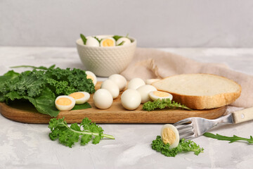 Wooden board with fresh boiled quail eggs, piece of bread and greens on light background