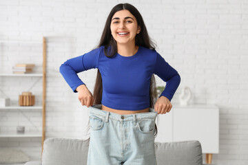 Beautiful young happy sporty woman in loose jeans at home. Weight loss concept