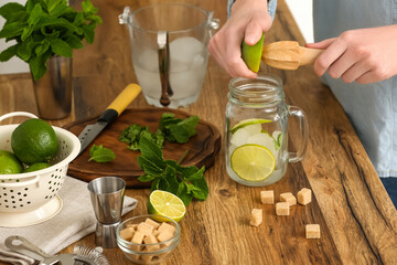 Young woman squeezing lime in jar with fresh mojito at home