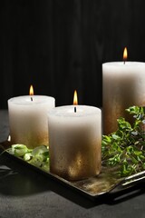 Burning candles and green leaves on black table, closeup