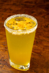 Refreshing passion fruit (maracuyá) cocktail or Lulada with a sugar rim and fresh seeds, an exotic tropical summer drink from Colombia served in a glass on a wooden bar.