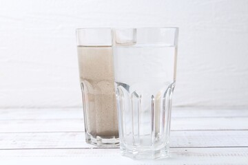 Glasses with clean and dirty water on white wooden table
