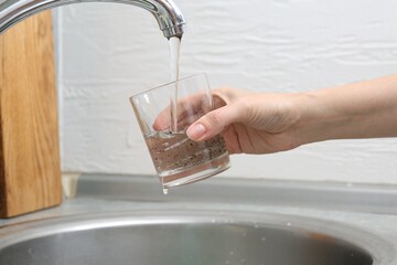 Woman filling glass with dirty tap water indoors, closeup