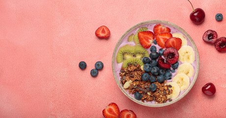 Vibrant and nutritious acai bowl topped with sliced kiwi, strawberries, blueberries, cherries, banana, and granola, a colorful and healthy meal or breakfast on a pink background, copy space