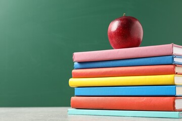 Different books and red apple on grey table against blackboard, low angle view. Space for text