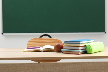Different school stationery and apple on wooden table near blackboard indoors