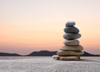 Stacked stones in a pyramid shape on a background of  sea, mountains and sunset, copy space for...