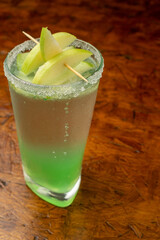 Refreshing Green Apple Martini (Appletini) cocktail with a sugar rim and fresh apple garnish, a layered alcoholic summer drink served in a highball glass on a dark wooden bar for happy hour.