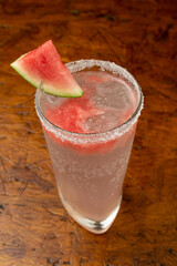 Close-up of a Refreshing Watermelon Cocktail with Salted Rim and Fresh Watermelon Slice Garnish on a Textured Wooden Table
