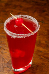 A classic red cherry cocktail with a sugar rim and maraschino garnish, a refreshing alcoholic beverage for a summer party at a bar, served in a glass on a wooden table.