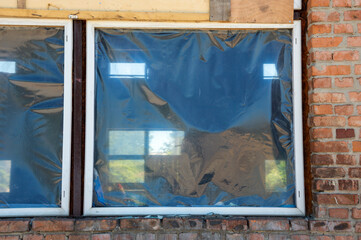 Renovation work is in progress as windows are covered with plastic sheeting in a brick building,...