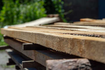 Wooden planks are neatly stacked on a sturdy workstation, bathed in daylight, with greenery in the...