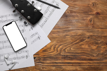 Music sheets with mobile phone, earphones and guitar on wooden background with space for text