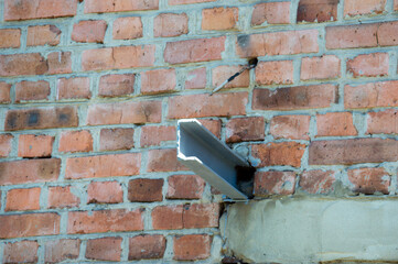 A section of a brick wall shows damage with an exposed metal beam jutting out, illuminated by...