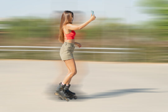 Young woman roller skating and taking a selfie with her smartphone in a park, with motion blur effect