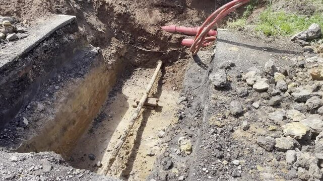 A construction site with exposed ground showing soil layers, red underground cables, and surrounding earthworks. Ideal for depicting infrastructure work, excavation projects