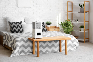 Interior of bedroom with shelving unit and modern humidifier on wooden bench near bed