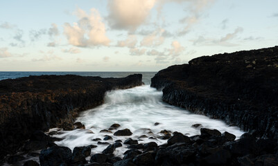 Waves flowing through a rocky channel on the coast of Kauai at sunset