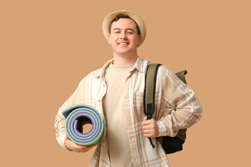 Fototapeta premium Young man with backpack and sleeping mat on brown background. Travel concept