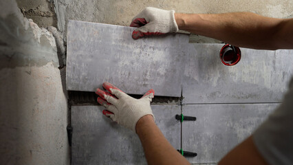 Professional construction worker carefully spreading cement glue on ceramic wall tiles during home...