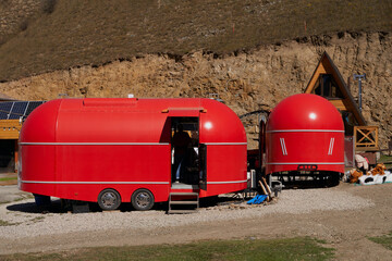 Two red food trucks at a campsite in the mountains.