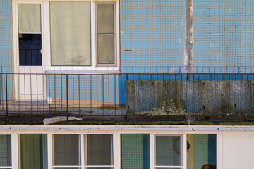 Close-up of a weathered blue apartment building showing peeling paint, rusted balcony railing, and...