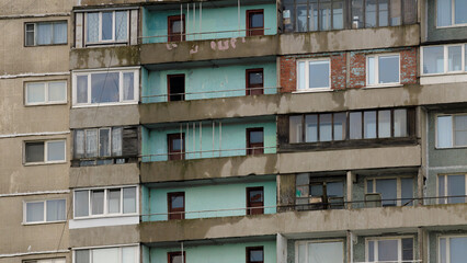 Detailed view of an old Soviet-era residential block with peeling paint, exposed brickwork, and deteriorating concrete balconies.