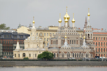 Skorbyashchenskaya Church in Saint Petersburg, featuring ornate architecture and golden onion domes, located by the riverside against historic buildings.