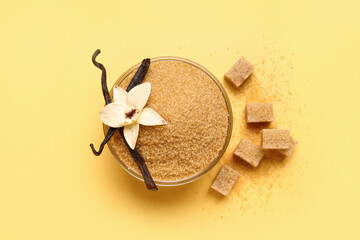 Glass bowl of vanilla sugar with pods and flower on yellow background