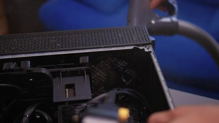 A man cleans a computer case with a vacuum in a bright room, stressing workspace tidiness