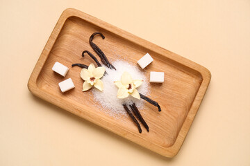 Wooden board of vanilla sugar with pods and flowers on beige background
