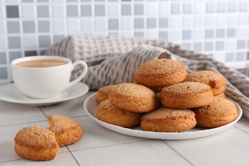 Plate with sweet cookies and cup of hot tea on white tile table