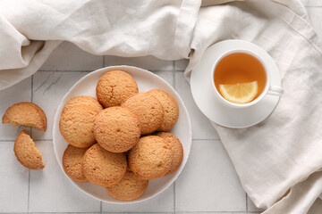 Plate with sweet cookies and cup of hot tea on white tile background