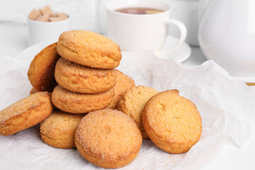 Baking paper with sweet cookies and cup of hot tea on white table, closeup